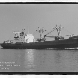 Schwarzweiß-Archivfoto eines Frachtschiffs mit Ladekränen und Deckshaus auf See; Logo Maritimes Museum Hamburg.