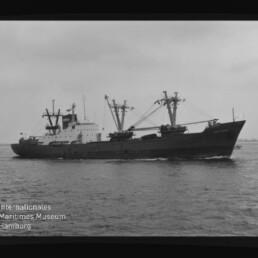 Frachtschiff mit mehreren Ladekränen auf See in einer Schwarzweißaufnahme, mit Schriftzug 'Internationales Maritimes Museum Hamburg' unten links.