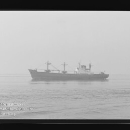 Schwarzweißaufnahme eines Frachtschiffs in ruhiger, diesiger See; Filmrand mit KODAK-Schriftzug und Wasserzeichen.