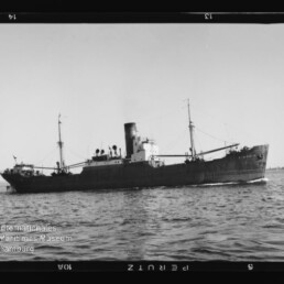 Schwarzweiß-Profil eines Frachtschiffs mit hohem Schornstein und Masten, fahrend auf ruhiger See; Museumslogo links unten.