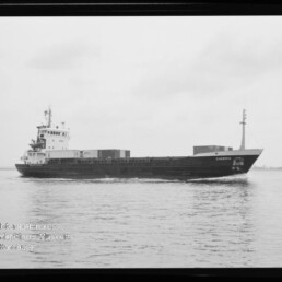 Frachtschiff CIMBRIA mit wenigen Containern auf ruhiger See, schwarzweiße Aufnahme mit Museumswasserzeichen links unten.