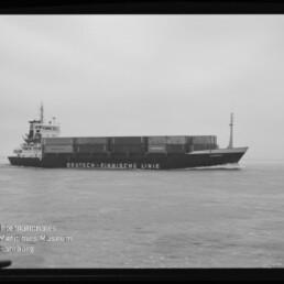 Schwarzweißfoto eines Containerschiffs mit der Aufschrift Deutsch-Finnische Linie auf ruhiger See, Stapelcontainer und Steuerhaus sichtbar.
