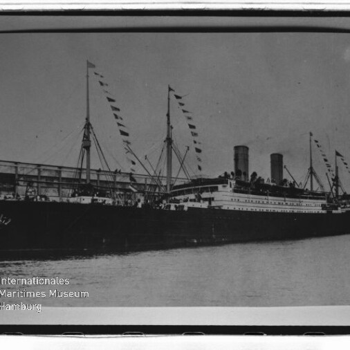 Dampfschiff mit zwei Schornsteinen und Festtagsflaggen am Kai, Personen auf dem Deck; Wasserzeichen Internationales Maritimes Museum Hamburg