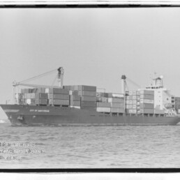 Schwarzweißaufnahme eines Containerschiffs City of Amsterdam mit gestapelten Containern und Deckskränen auf hoher See.