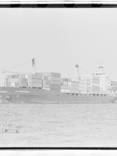 Containerschiff mit gestapelten Containern auf ruhiger See; Wasserzeichen des Internationalen Maritimen Museums Hamburg.