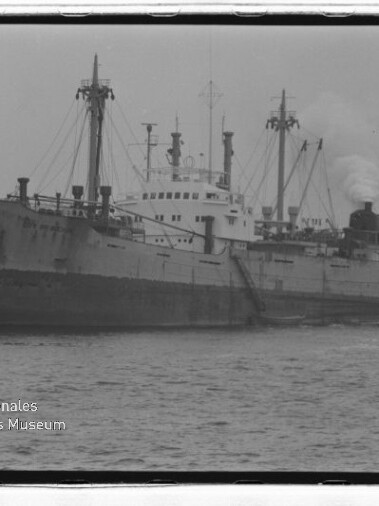 Großes Frachtschiff mit Masten und rauchendem Schornstein im Hafen; Wasserzeichen des Internationalen Maritimen Museums Hamburg