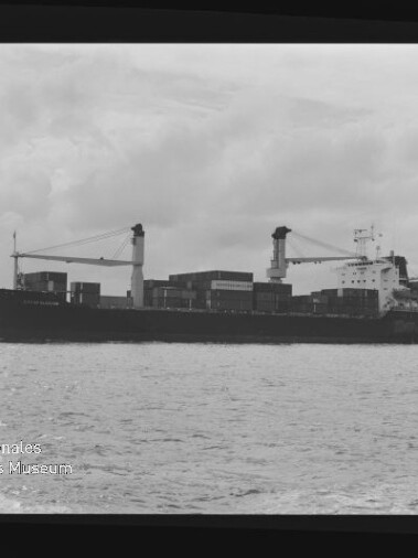 Schwarzweiß-Seitenansicht eines Containerschiffs mit Deckskranen und Containern auf ruhiger See, Museumswasserzeichen links unten.