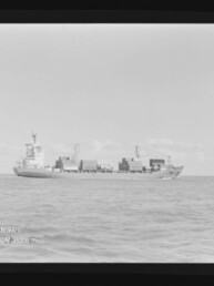 Schwarzweiß-Foto eines Containerschiffs mit gestapelten Containern auf ruhiger See, Filmrand und Museumswasserzeichen.