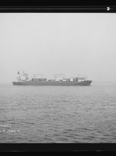 Containerschiff auf ruhiger, nebliger See am Horizont; linkes unteres Wasserzeichen Internationales Maritimes Museum Hamburg