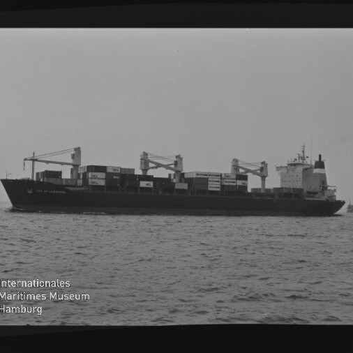Containerschiff mit geladenen Containerstapeln und Ladekränen auf ruhiger See; Museumslogo unten links.