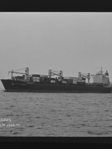 Schwarzweiß-Seitenansicht eines Containerschiffs mit gestapelten Containerboxen und Ladekränen auf ruhiger See.