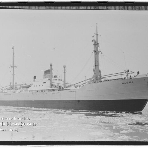 Frachtschiff Algol in teilweise vereistem Wasser, Seitenansicht mit hohen Masten, Brückenaufbau und gut lesbarem Schiffsname.