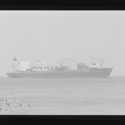 Frachtschiff mit Containern und Deckkränen auf ruhiger See, blasses Negativ mit Wasserzeichen 