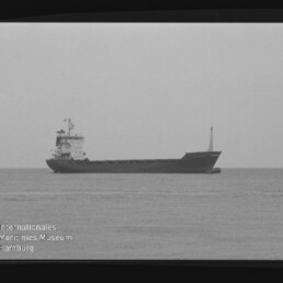 Frachtschiff seitlich auf ruhiger See, Schwarzweißaufnahme mit Filmrand und Museumssignet Maritimes Museum Hamburg