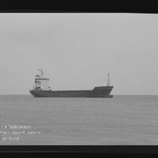 Schwarzweißaufnahme eines Frachtschiffs in Seitenansicht auf ruhiger See, mit sichtbarem Filmrand und Wasserzeichen des Internationalen Maritimen Museums Hamburg
