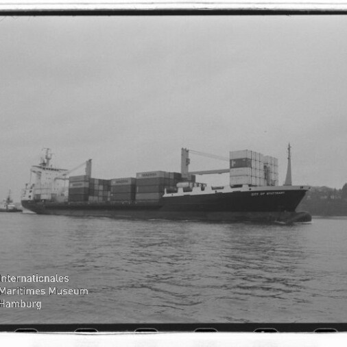 Schwarzweißfoto eines Containerschiffs mit gestapelten Containern und Ladekränen vor einem Ufer, mit Signet Internationales Maritimes Museum Hamburg.