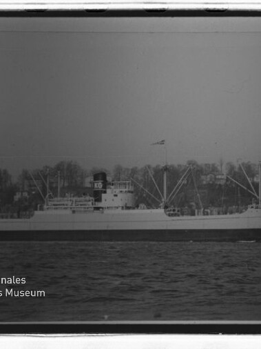 Frachtschiff in Seitenansicht auf See, mit Ladekränen und markantem Schornstein mit den Buchstaben KG