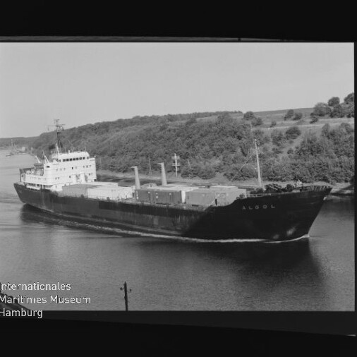 Frachtschiff mit Namenszug am Bug auf einem Kanal vor bewaldetem Ufer, mit Wasserzeichen des Int. Maritimen Museums Hamburg