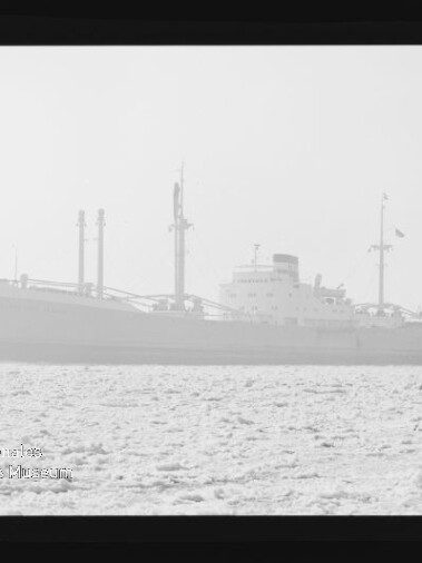 Frachtschiff mit sichtbaren Ladekränen auf nebliger, kontrastarmer See, Filmrahmen und Museumswasserzeichen am Rand sichtbar.