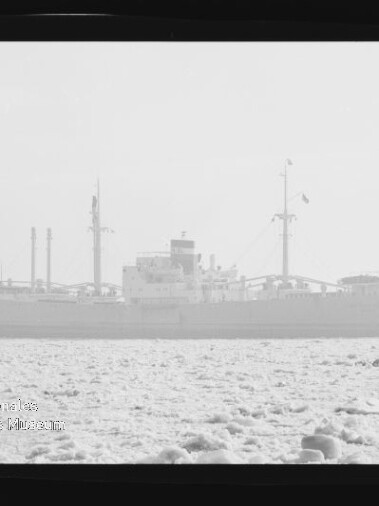 Großes Frachtschiff als verschwommene Silhouette auf ruhiger See, im Vordergrund treibende Eisschollen