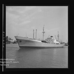 Schwarzweiß-Aufnahme eines Frachtschiffs namens Clipper Stevens im Hafen, Seitenansicht mit Ladebäumen