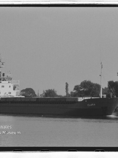 Frachtschiff CLARA auf einem Kanal vor baumbewachsenem Ufer, schwarzweiß-Aufnahme mit Museumslogo unten links.