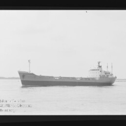 Frachtschiff in Seitenansicht auf ruhiger See, schwarz-weißes Foto mit sichtbarem Museumslogo unten links.