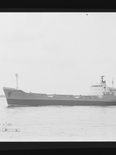 Frachtschiff in Seitenansicht auf ruhiger See, schwarz-weißes Foto mit sichtbarem Museumslogo unten links.