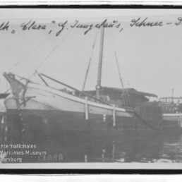 Segelschiff „Clara“ am Hafensteg, Seitenansicht mit Mast und Spiegelung im Wasser, handschriftliche Beschriftung oben