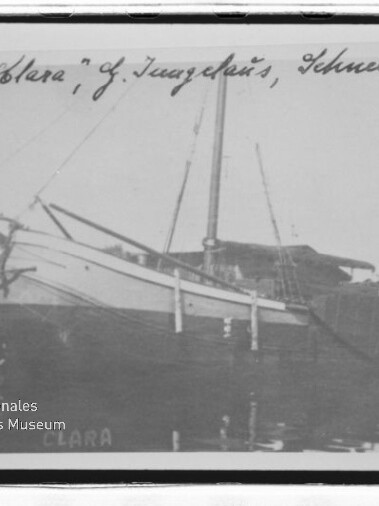 Segelschiff „Clara“ am Hafensteg, Seitenansicht mit Mast und Spiegelung im Wasser, handschriftliche Beschriftung oben