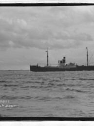 Dampffrachter mit Schornstein und Masten auf ruhiger See unter wolkigem Himmel, Museumslogo unten links.