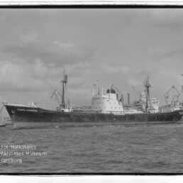 Frachtschiff Claudia Schneider im Hafen vor Ladekränen, schwarzweiß, Wasser im Vordergrund und Museumswasserzeichen