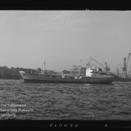 Frachtschiff auf der Elbe vor dem Hamburger Hafen mit mehreren Hafenkränen und leicht welliger Wasseroberfläche.