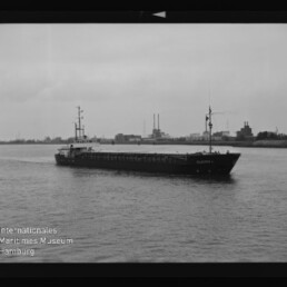 Frachtschiff „CLAUDIA K.“ fährt auf ruhigem Fluss, im Hintergrund Industrieanlagen mit hohen Schornsteinen