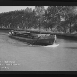 Binnenschiff Claudia fährt auf einem Kanal, Ufer mit einer Baumreihe im Hintergrund.