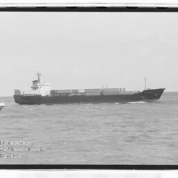 Frachtschiff seitliche Ansicht auf dem Meer mit Containerladung auf dem Deck und kleinem Begleitboot links