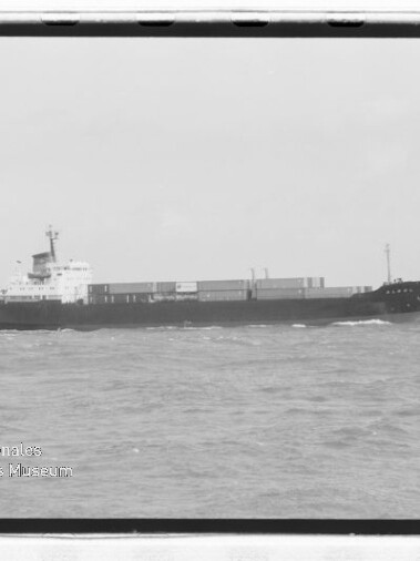 Frachtschiff seitliche Ansicht auf dem Meer mit Containerladung auf dem Deck und kleinem Begleitboot links