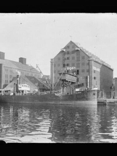 Frachtschiff Claris am Industriequai vor großen Speichergebäuden mit Krananlagen, Spiegelung im Wasser.