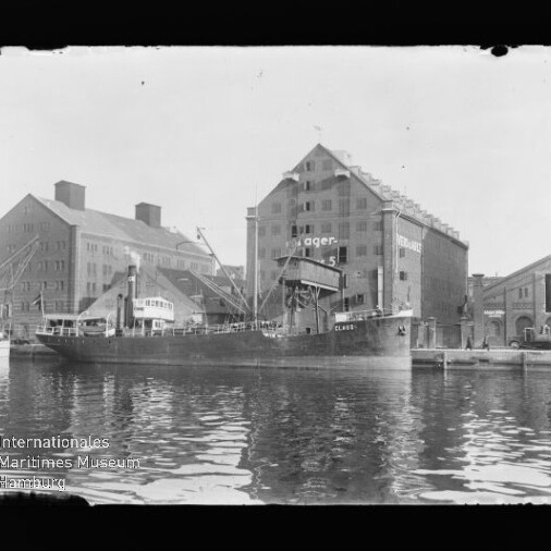 Frachtschiff Claris am Industriequai vor großen Speichergebäuden mit Krananlagen, Spiegelung im Wasser.
