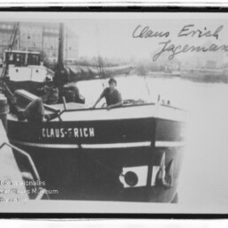 Schwarzweißfoto eines Kahns namens Claus Erich mit Person an Deck am Kanalufer; handschriftlicher Name oben rechts.