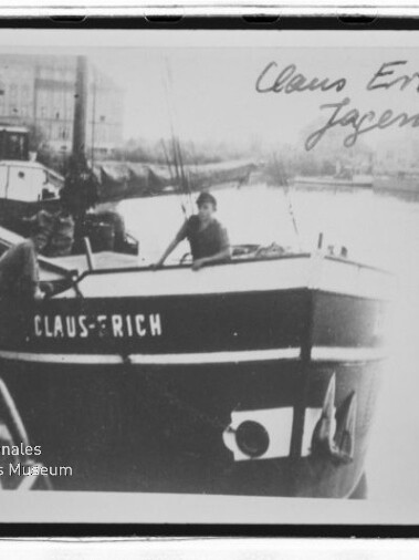 Schwarzweißfoto eines Kahns namens Claus Erich mit Person an Deck am Kanalufer; handschriftlicher Name oben rechts.