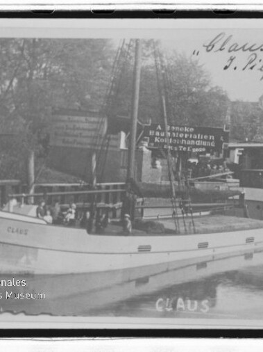 Schwarzweiß-Foto eines Frachtseglers Claus mit Mast und Namen am Bug, vertäut im Hafen; Museumswasserzeichen sichtbar.
