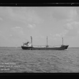Schwarzweiß-Foto eines Frachtschiffs auf ruhiger See; unten links Logo Int. Maritimes Museum Hamburg.