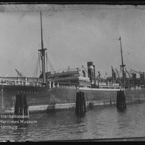 Frachtschiff mit Masten und Schornstein am Kai, Pfähle im Wasser und Logo Internationales Maritimes Museum Hamburg