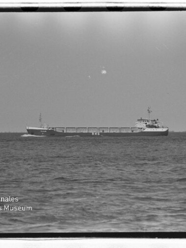 Frachtschiff auf ruhiger See am Horizont, Schwarzweißaufnahme mit Museums-Wasserzeichen unten links.
