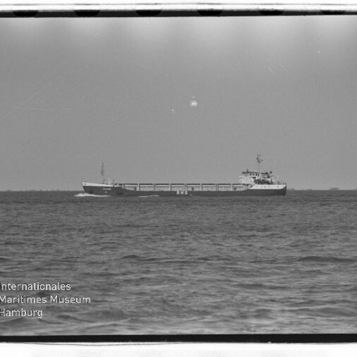 Frachtschiff auf ruhiger See am Horizont, Schwarzweißaufnahme mit Museums-Wasserzeichen unten links.