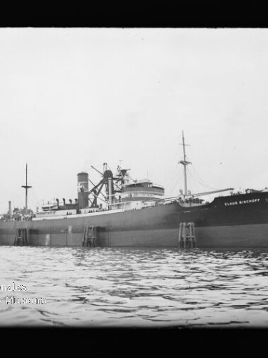 Großes Frachtschiff am Kai mit sichtbaren Aufbauten, Masten und ruhiger Wasserfläche im Vordergrund