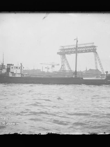 Schwarzweißfoto: Frachtschiff auf dem Wasser vor großen Hafenkränen; Wasserzeichen des Internationalen Maritimen Museums Hamburg.