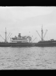 Schwarzweiß-Foto eines Passagier- und Frachtschiffs mit Schornstein und Ladekränen auf ruhiger See.