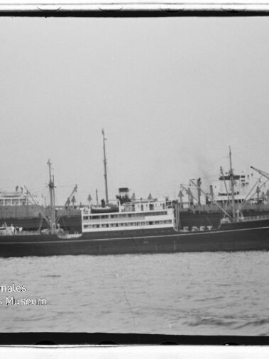 Schwarzweißaufnahme eines Frachtschiffs mit Aufbauten und Hafenkränen, Wasserzeichen Internationales Maritimes Museum Hamburg.